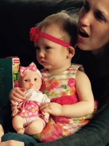 toddler holding baby doll sitting on mother's lap Providence Moms Blog
