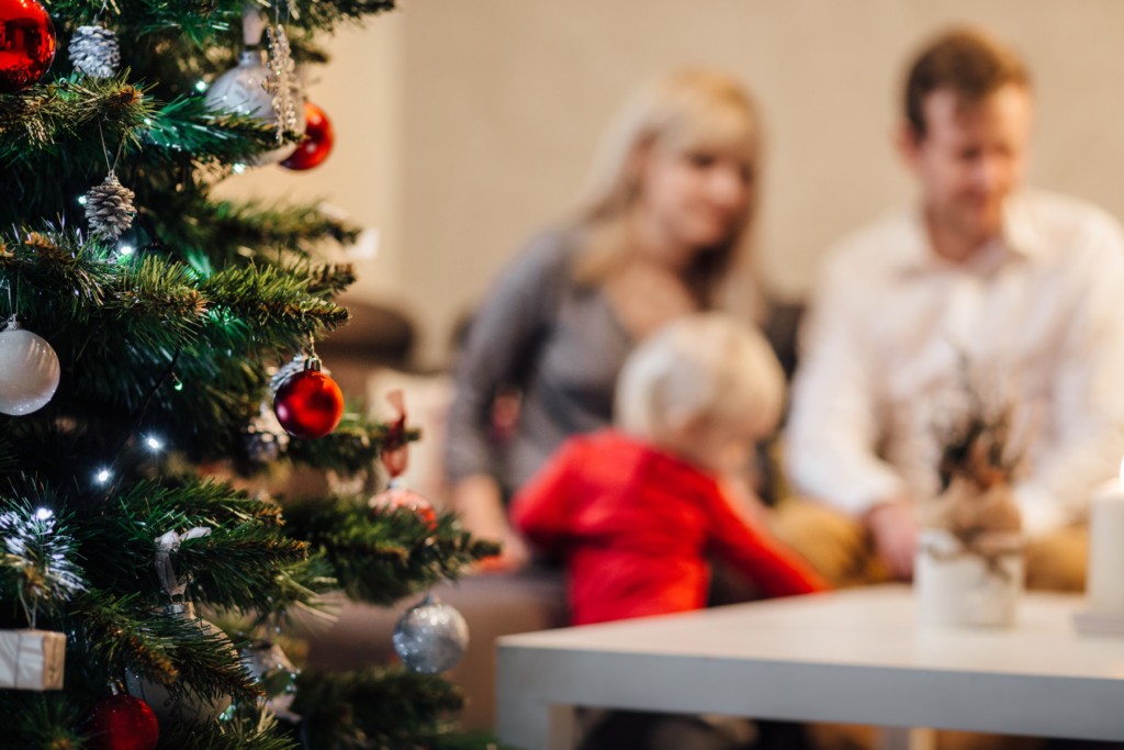 Decorated Christmas Tree with blurry blond headed small child and two adults in the background. Picture in Providence Moms Blog Post on Holiday Stress