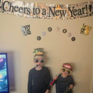 Noon year's eve party decorations: Kids with crows and noisemakers under "Cheers to a New Year" sign