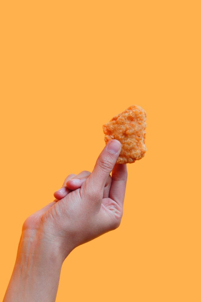 Hand holding a chicken nugget against an orange background in picky eating article