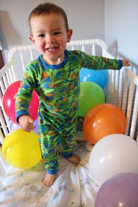 toddler in crib with birthday balloons