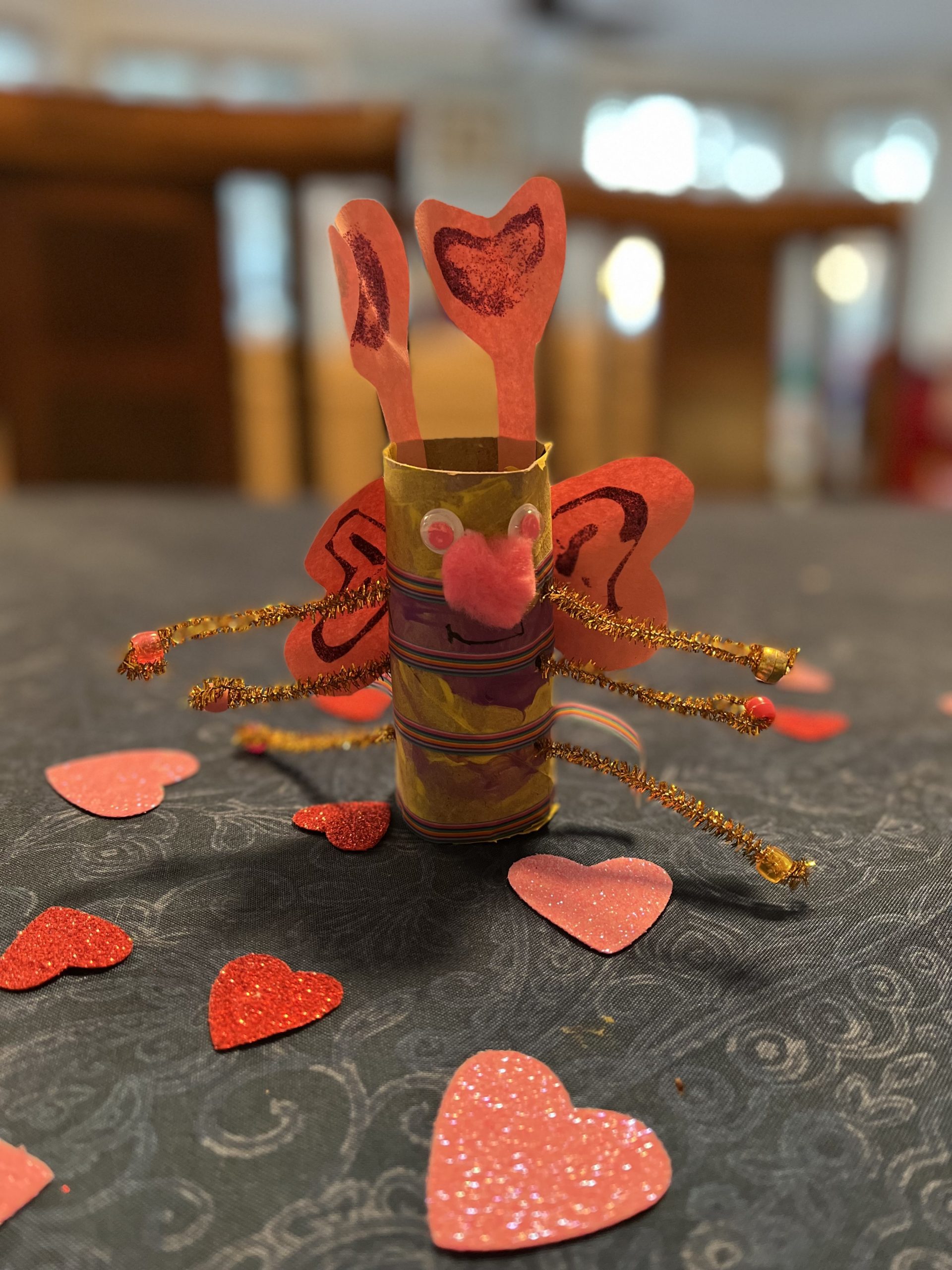 A cardboard roll with pipe cleaners coming out of the sides like arms and painted to look like a bug with paper antennae and wings