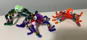 A green, purple and orange pipe cleaner spider with beads threaded on the legs, pom poms for heads and googly eyes