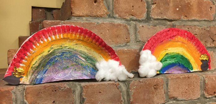 Two halves of a cardboard plate painted to resemble rainbows