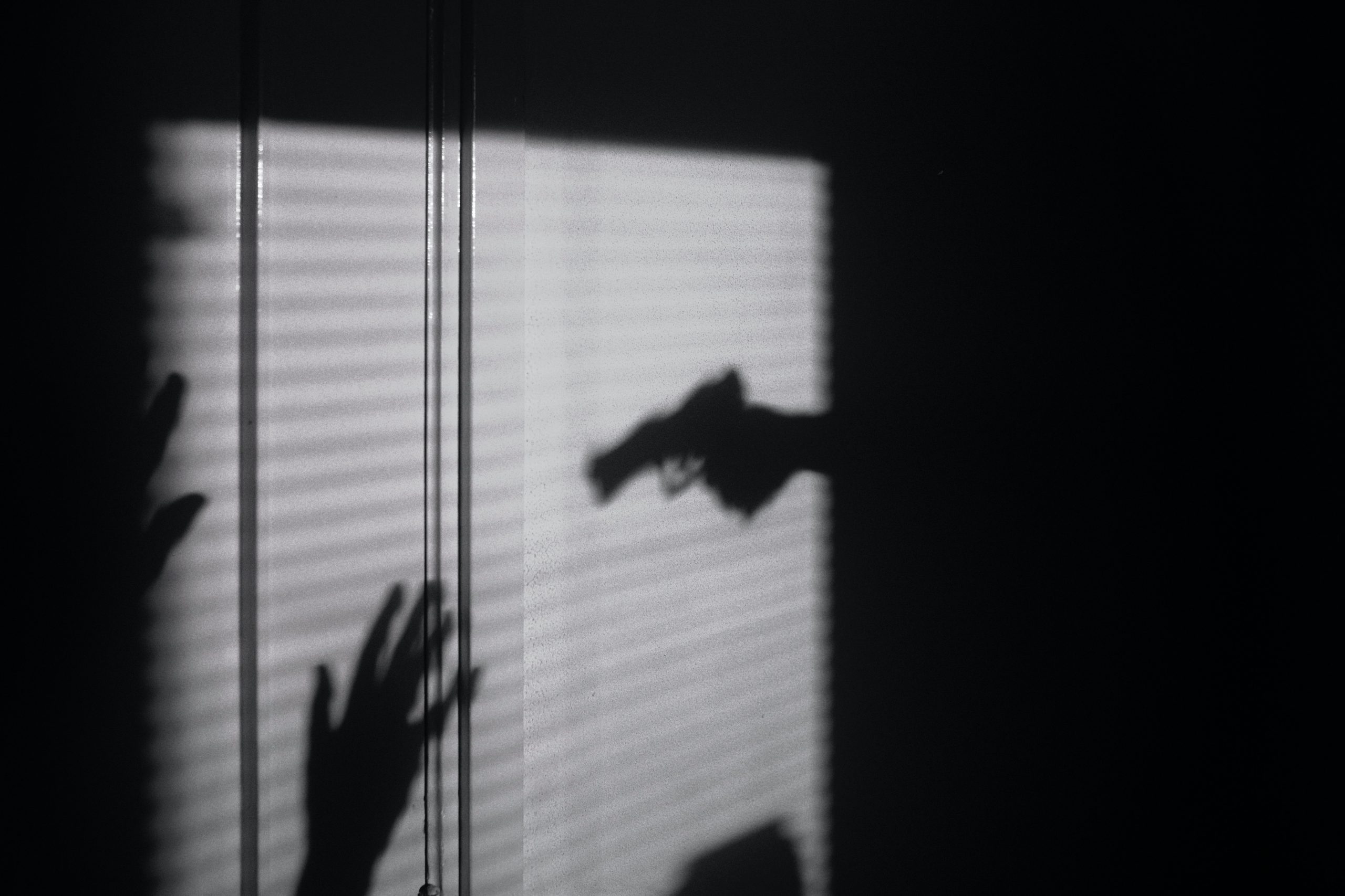 Shadow of a hand pointing a gun at raised hands 