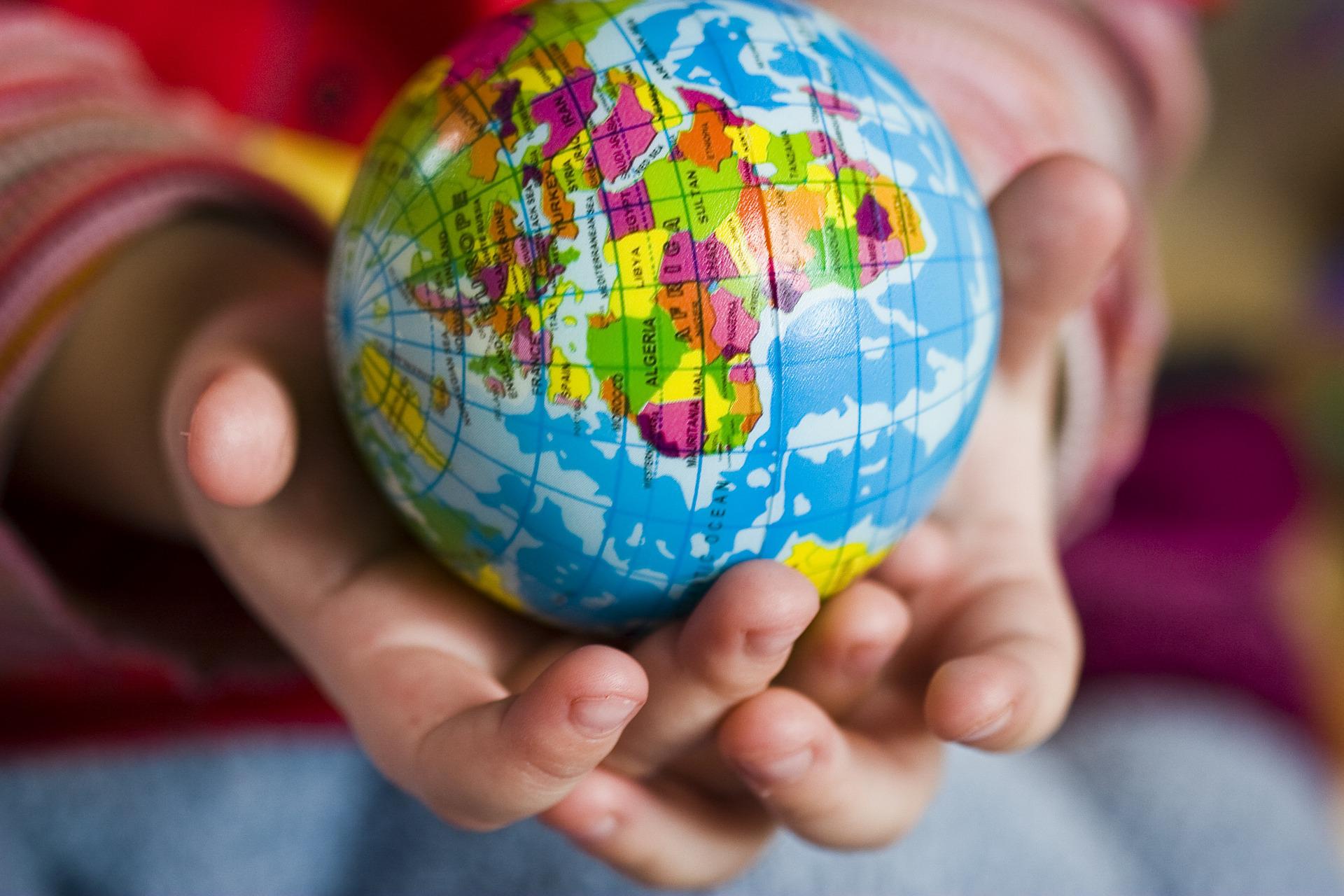 A small ball with the globe printed on it sits in a pair of hands that look like they belong to a small child
