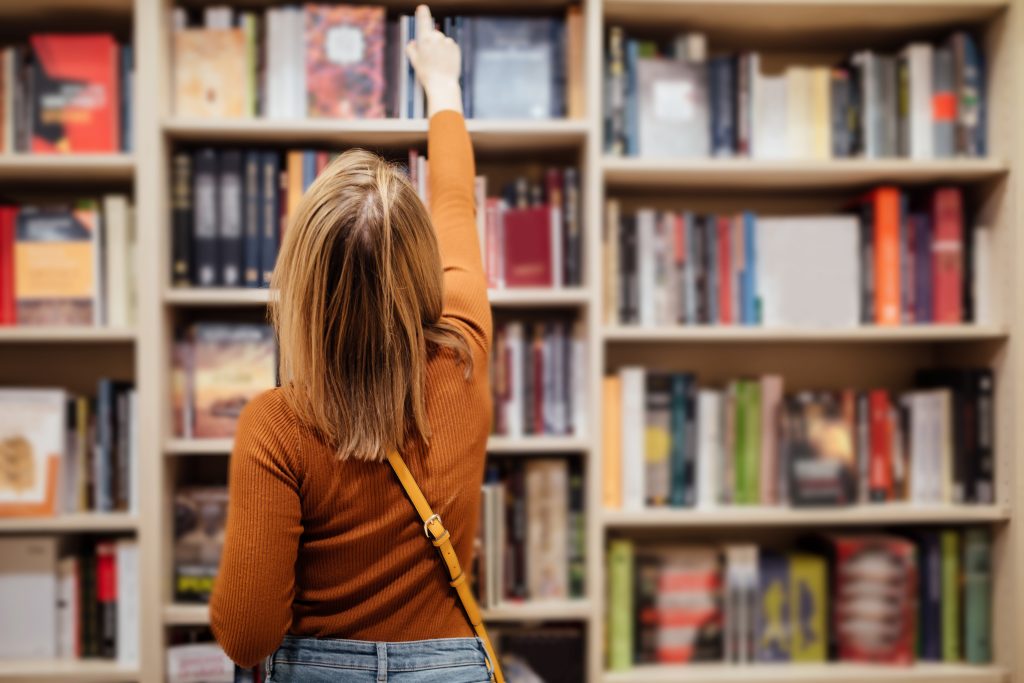 woman choosing a book from a bookstore shelf